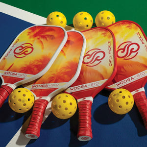 Four Chill Pickle Woosa pickleball paddles arranged on a court with yellow balls