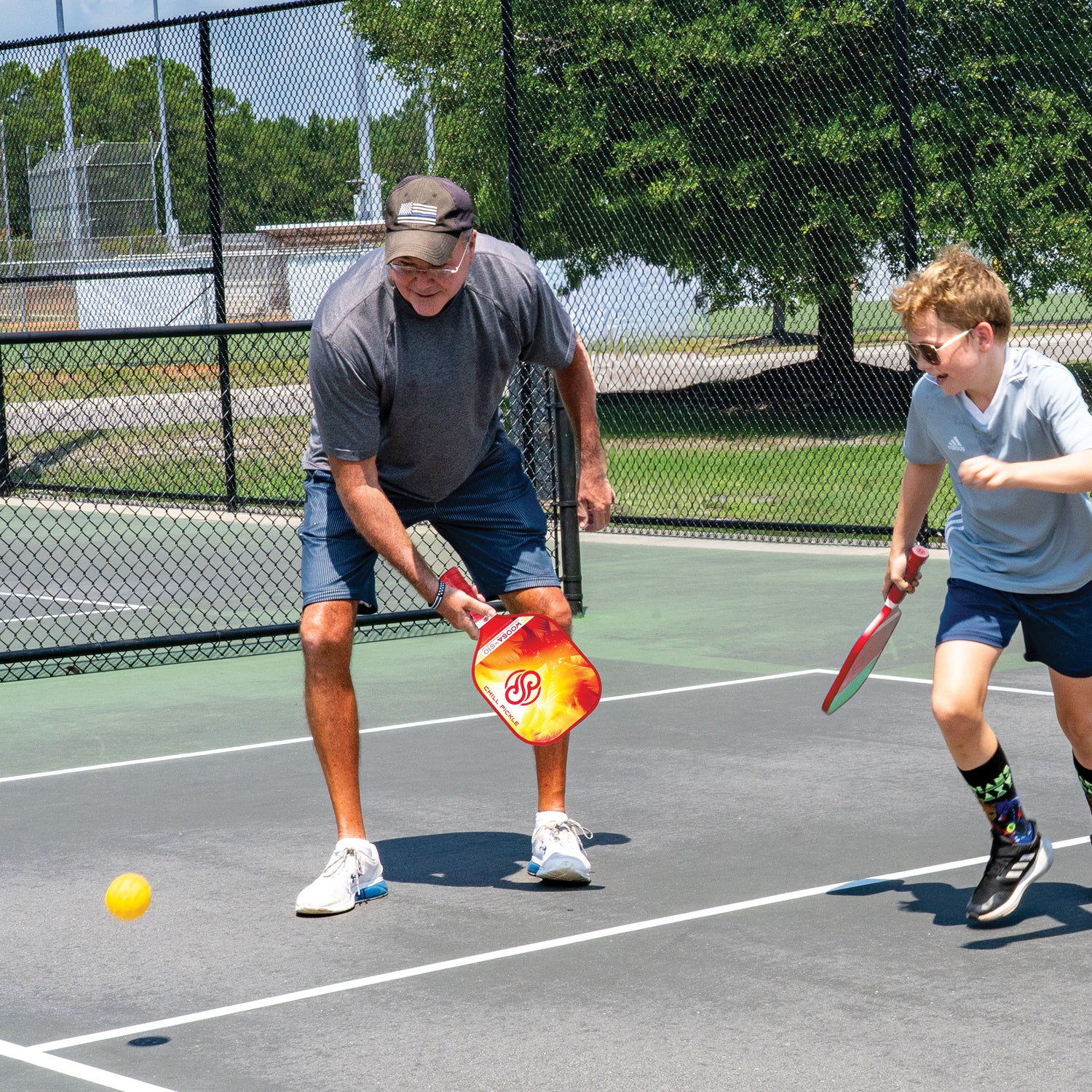 Grandfather and child playing pickleball together on an outdoor court with Chill Pickle paddles