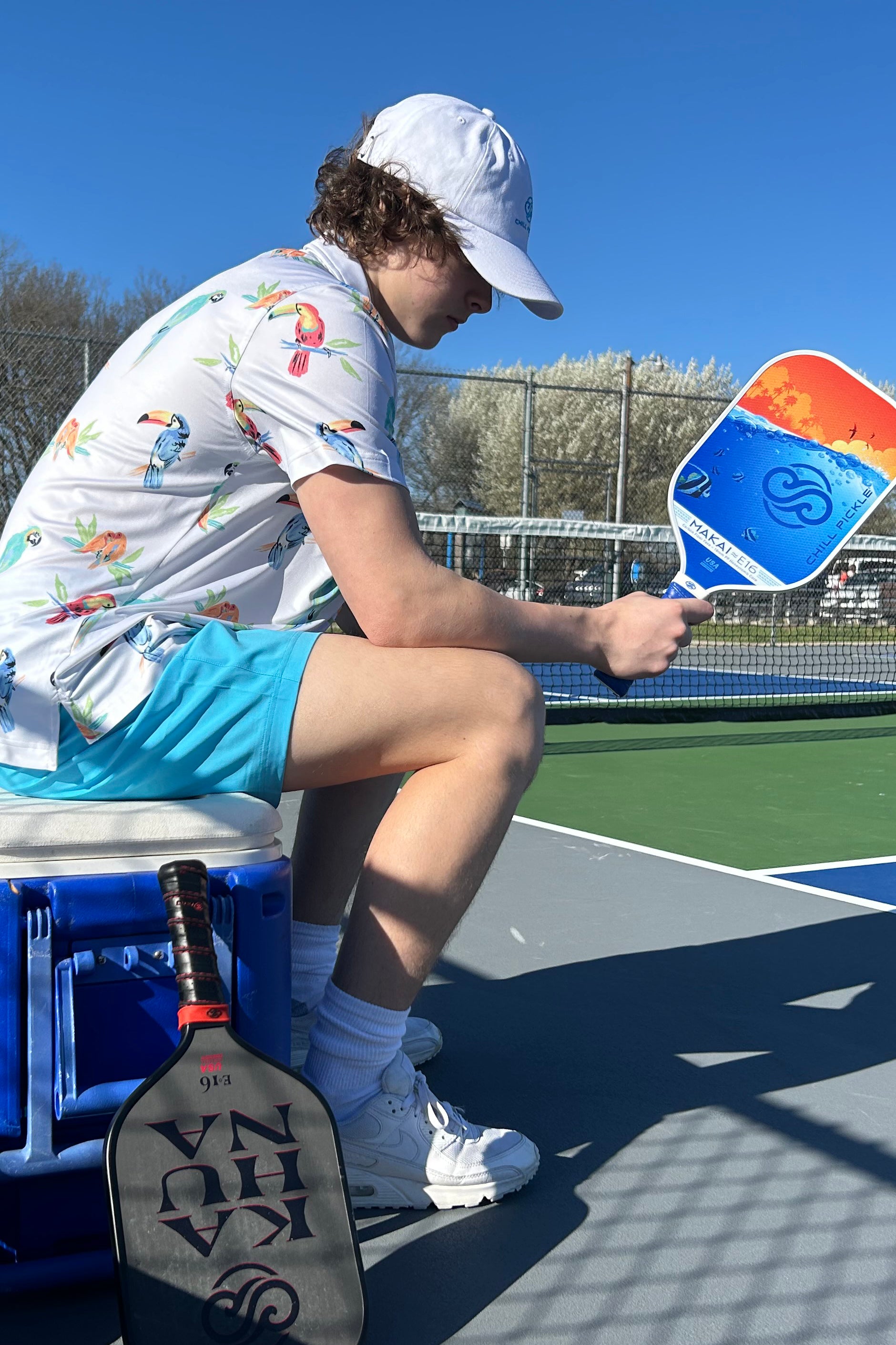 Pickleball player sitting on a cooler holding a Chill Pickle Makai paddle courtside