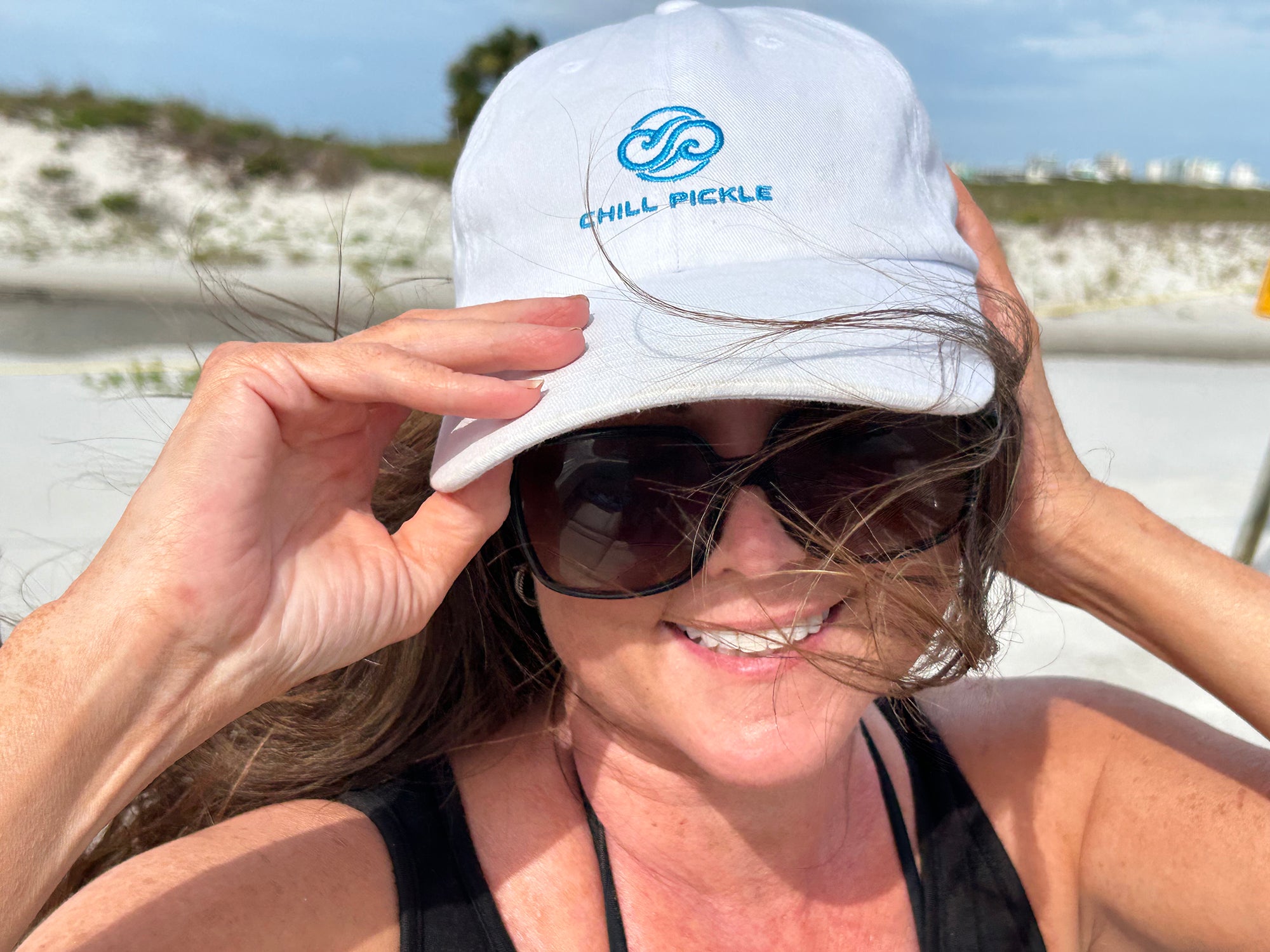 Woman wearing a white Chill Pickle baseball cap outdoors in sunny beachside setting