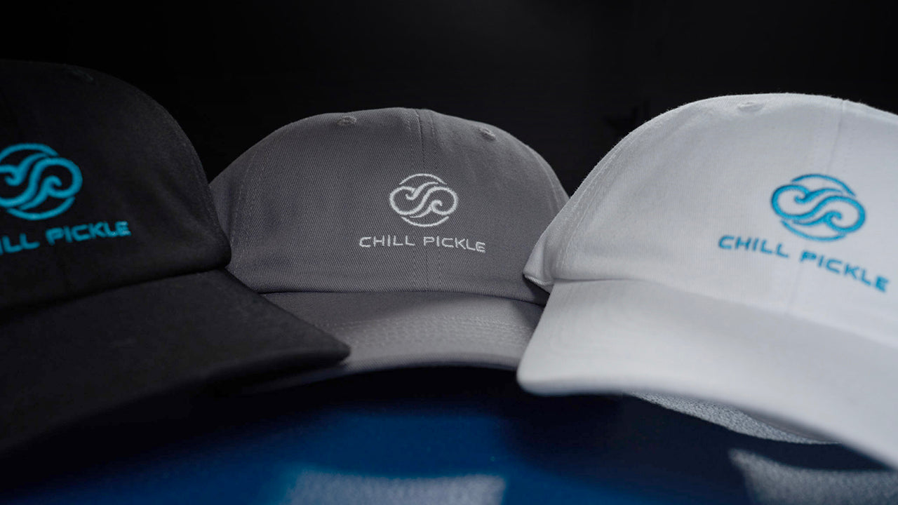 Three pickleball caps with Chill Pickle logo on a dark background