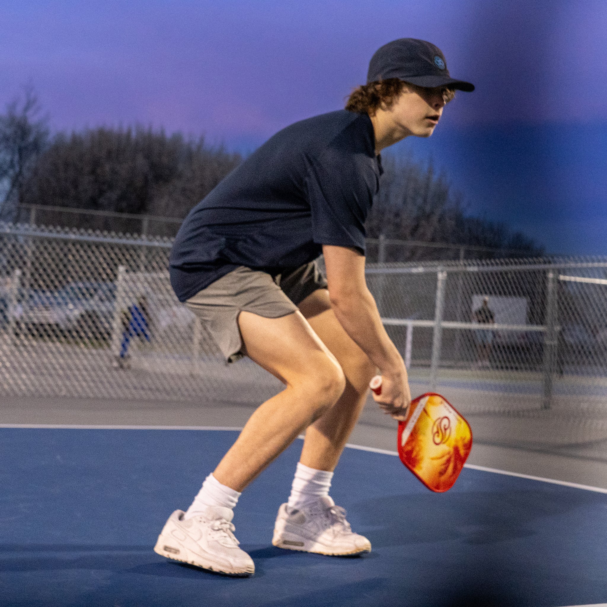 Player executing a soft dink shot under evening lighting on an outdoor court