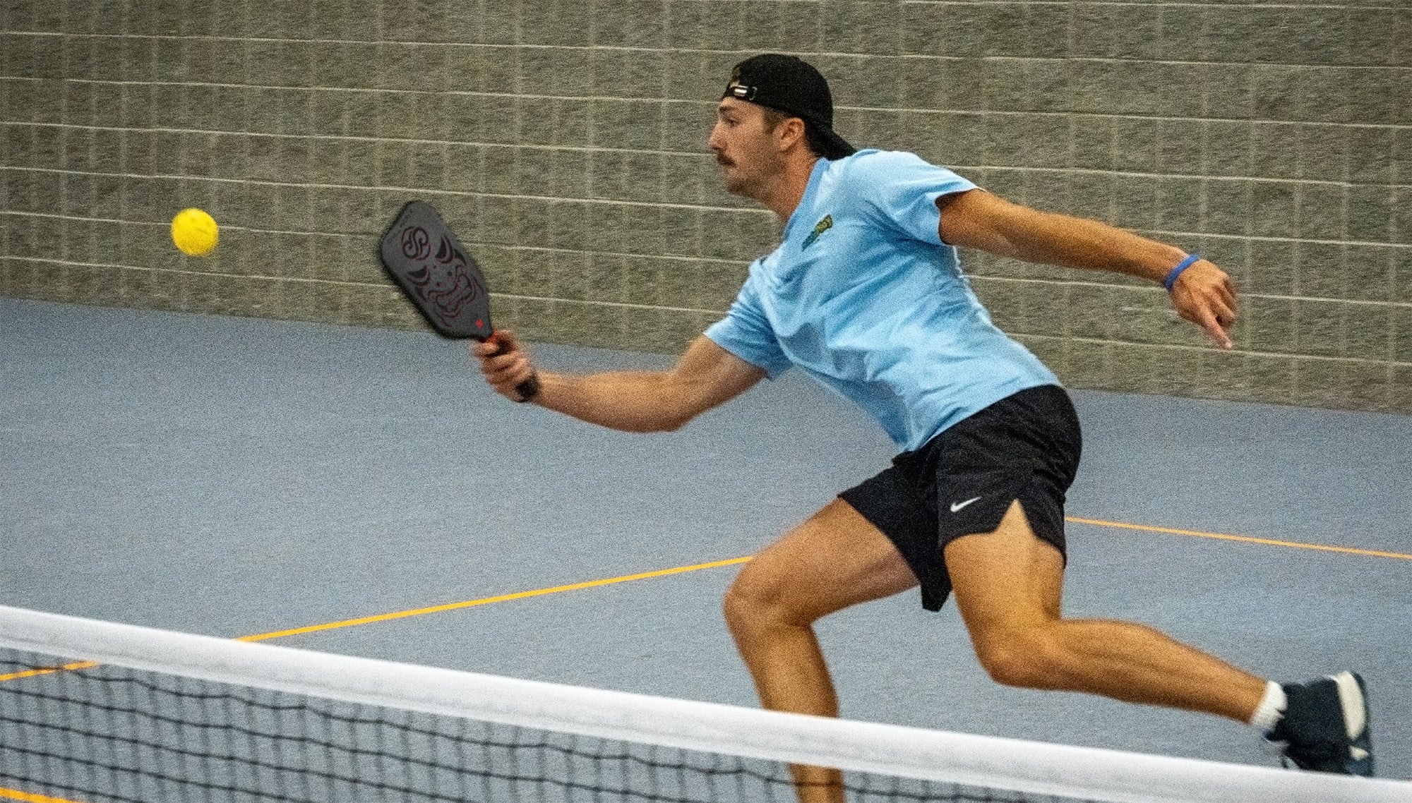 Pickleball athlete sprinting forward to return a fast shot on an indoor court