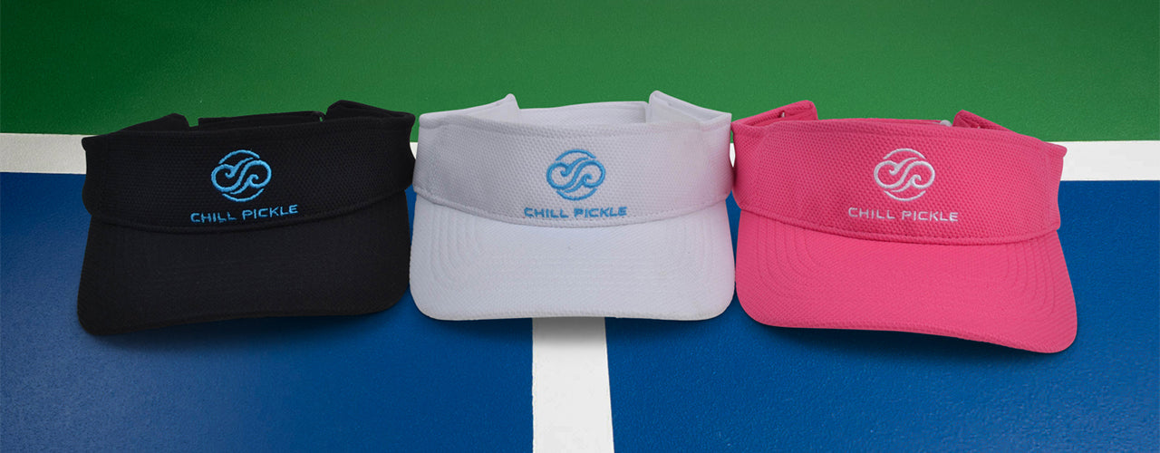 Three visors in black, white, and pink on a pickleball court background with Chill Pickle branding.