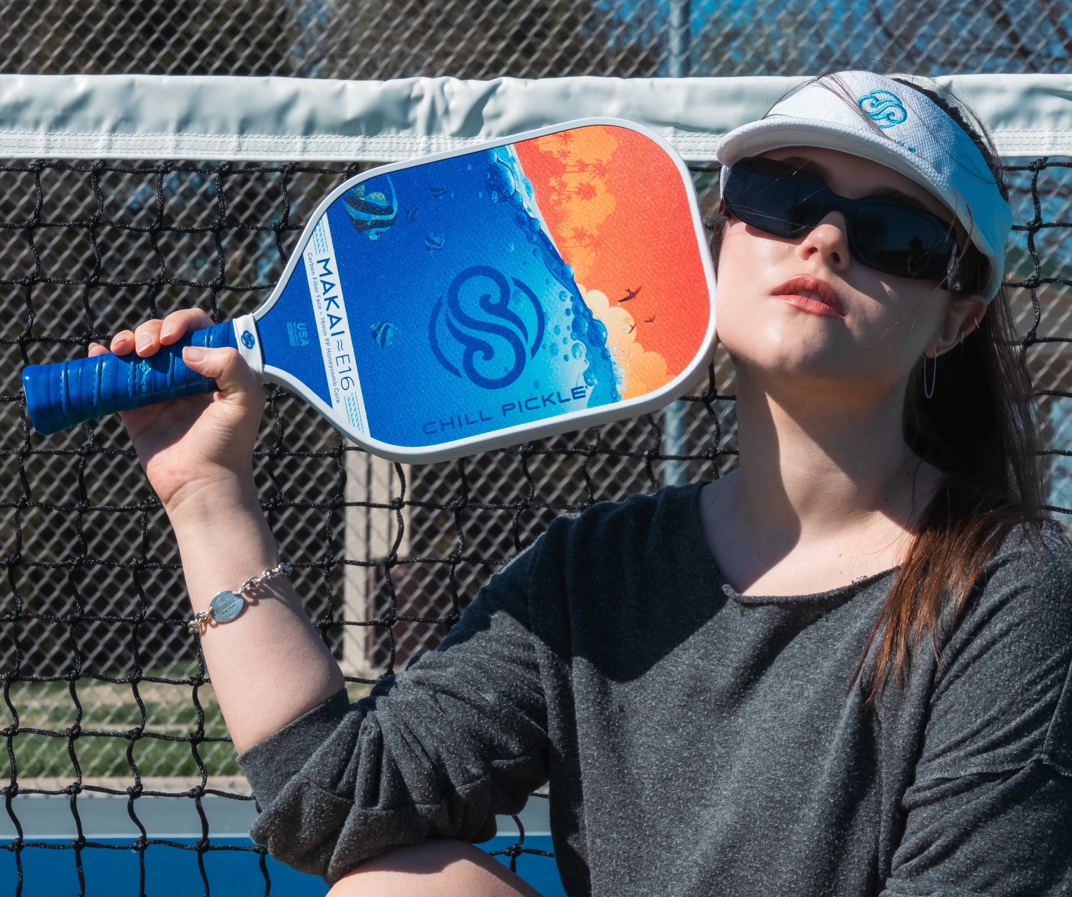 Girl posing with a Chill Pickle Makai pickleball paddle on a court with a net in the background