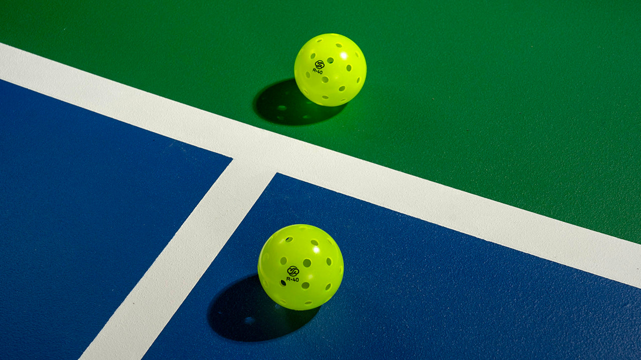 Two yellow pickleballs resting on the painted lines of an outdoor court